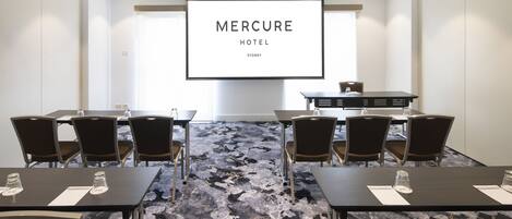 A conference room with a large screen displaying 'Mercure Hotel Sydney' and a carpeted floor.