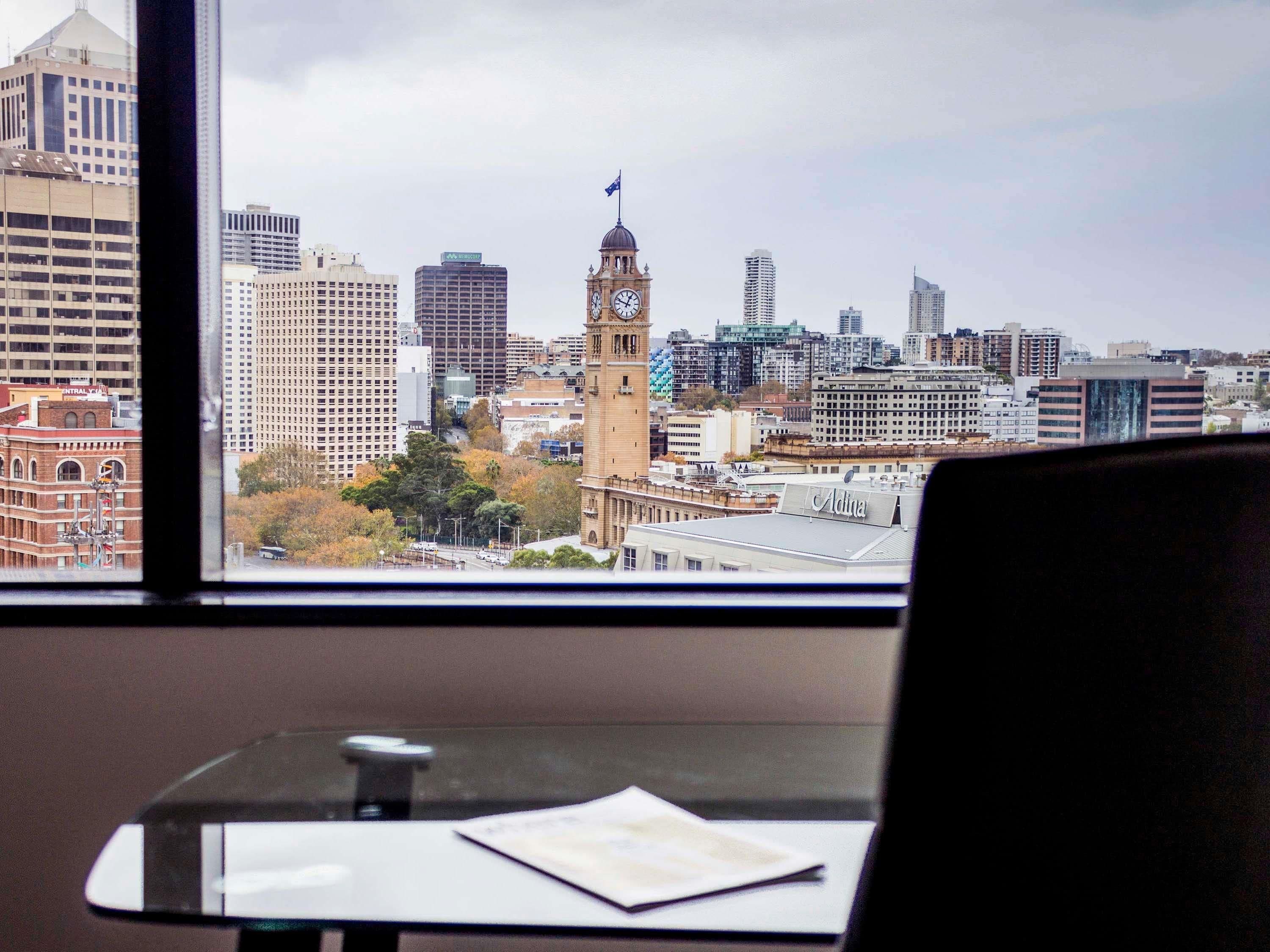 A view of a cityscape with a prominent clock tower, modern buildings, and a table with a cup and a piece of paper.