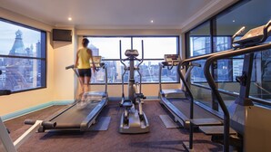A gym with treadmills, an elliptical, and a rowing machine, featuring large windows with a city view. - Mercure Sydney (Chippendale)
