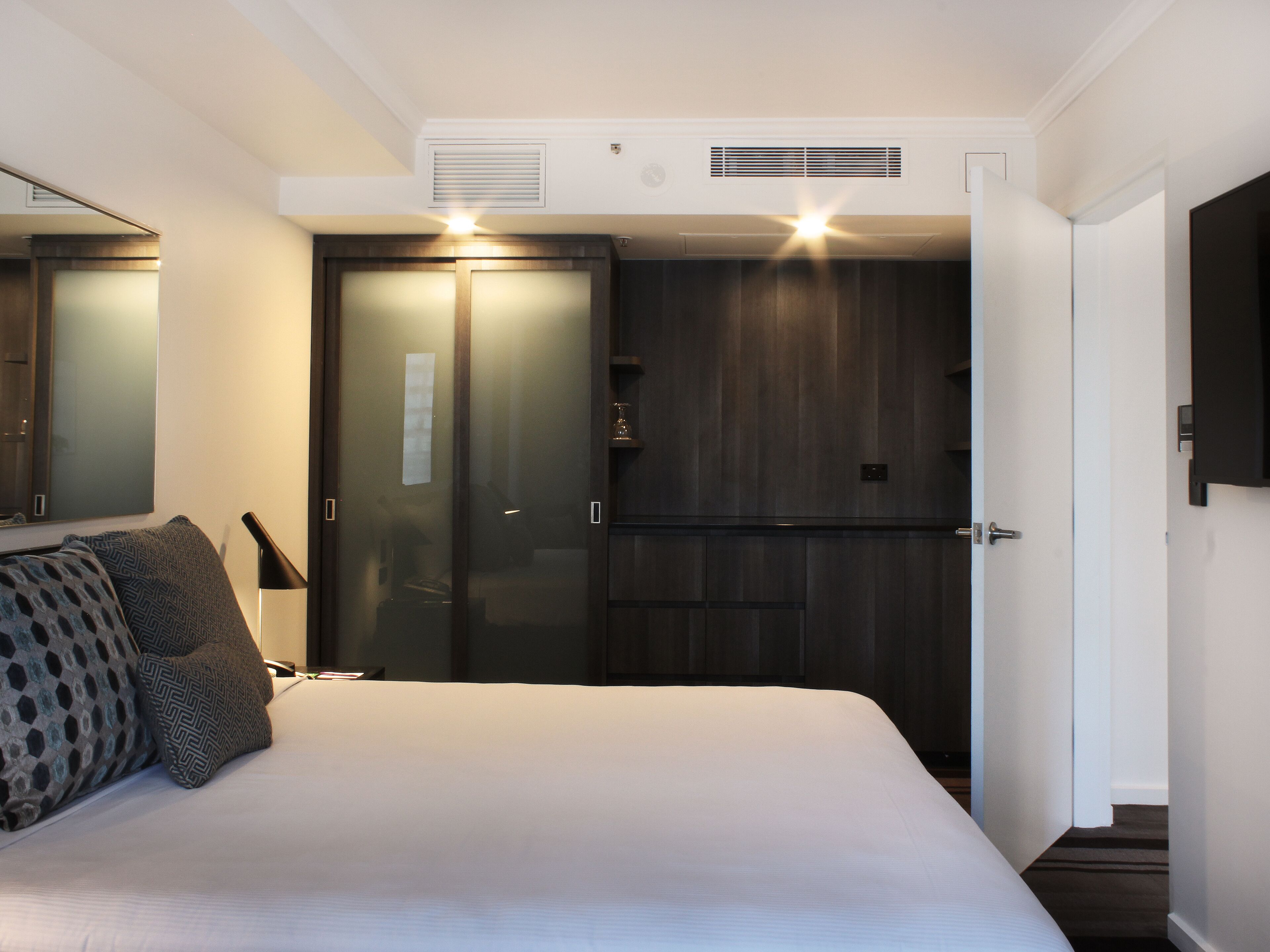 Et soveværelse med seng, natbord, lampe, garderobeskab og spejl.