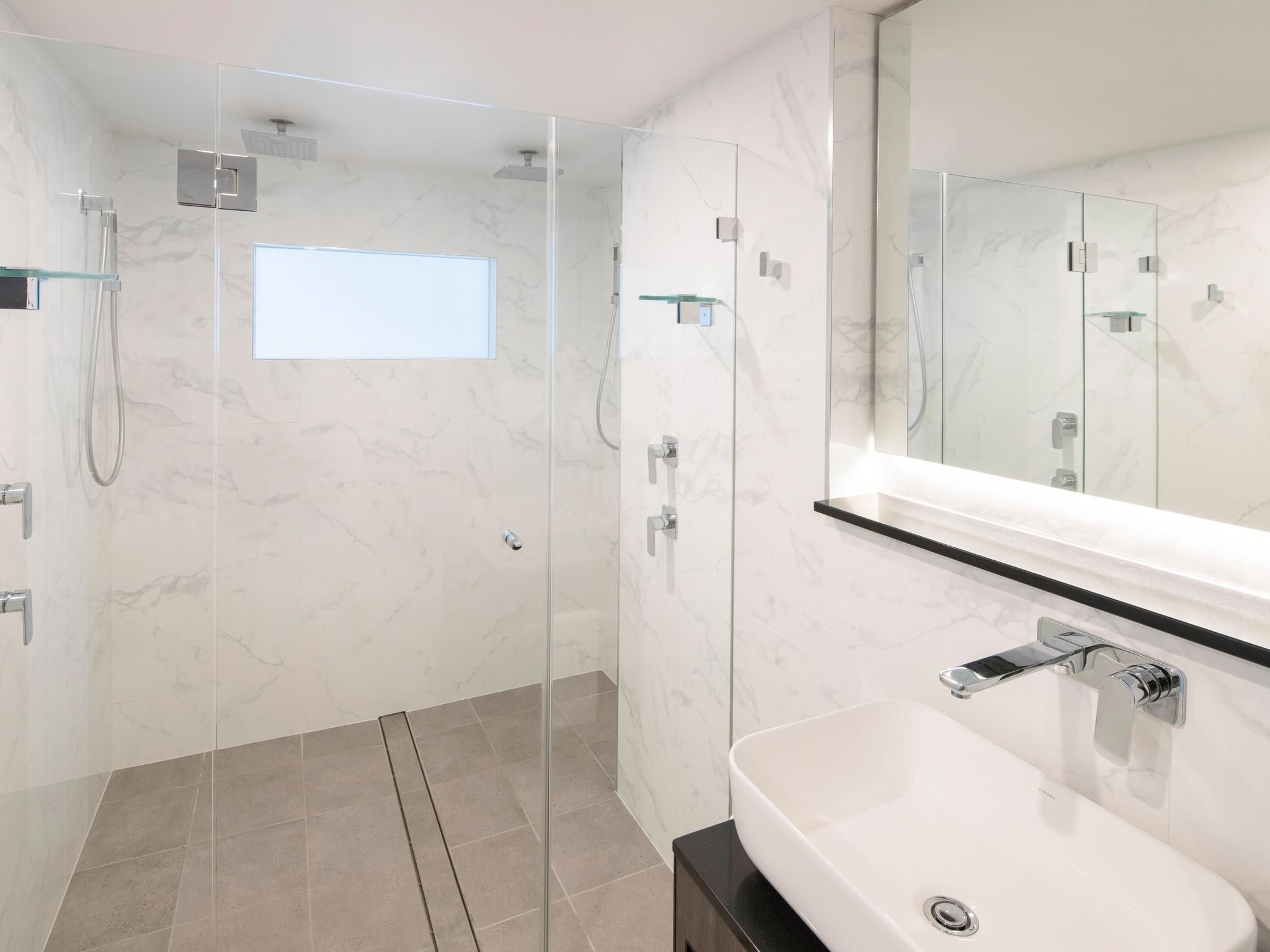 A modern bathroom with a glass-enclosed shower, a white sink, and a large mirror.