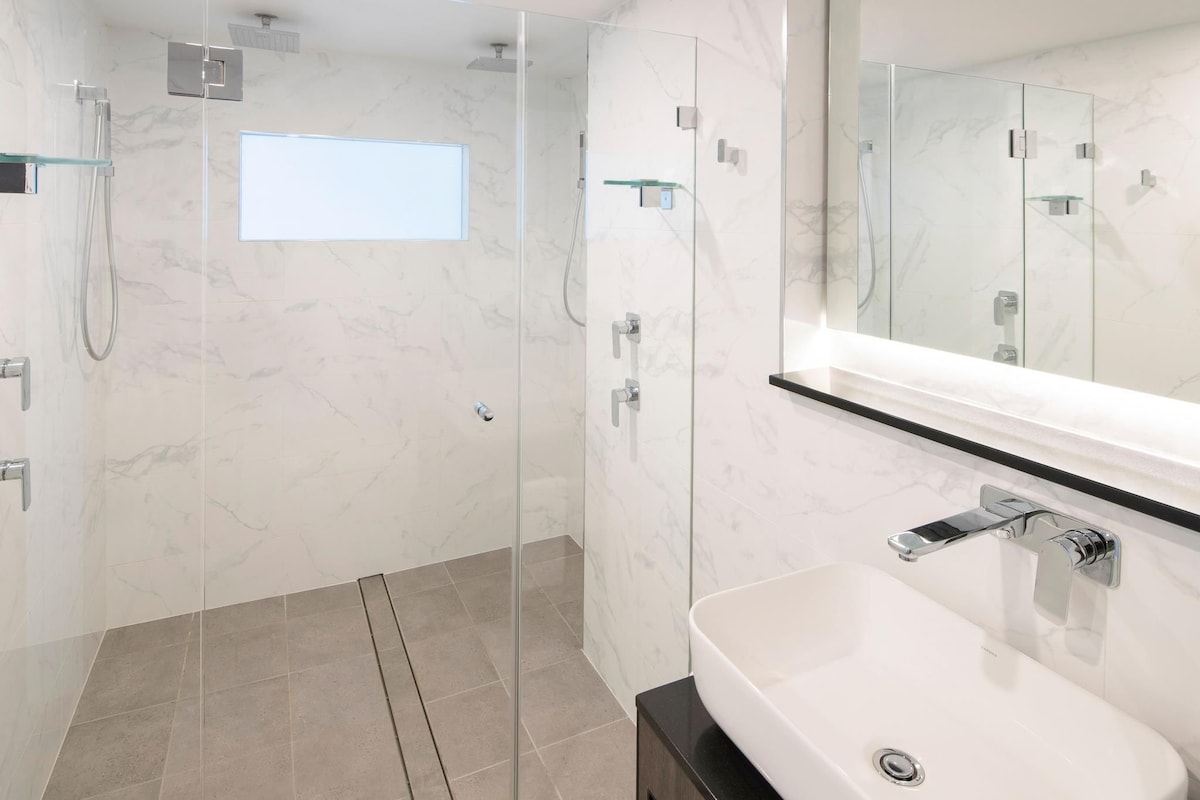 Une salle de bain moderne avec une douche à parois de verre, un lavabo blanc et un grand miroir.