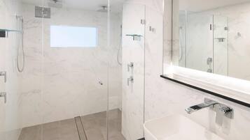 Ein modernes Badezimmer mit einer in Glas eingefassten Dusche, einem weißen Waschbecken und einem großen Spiegel.