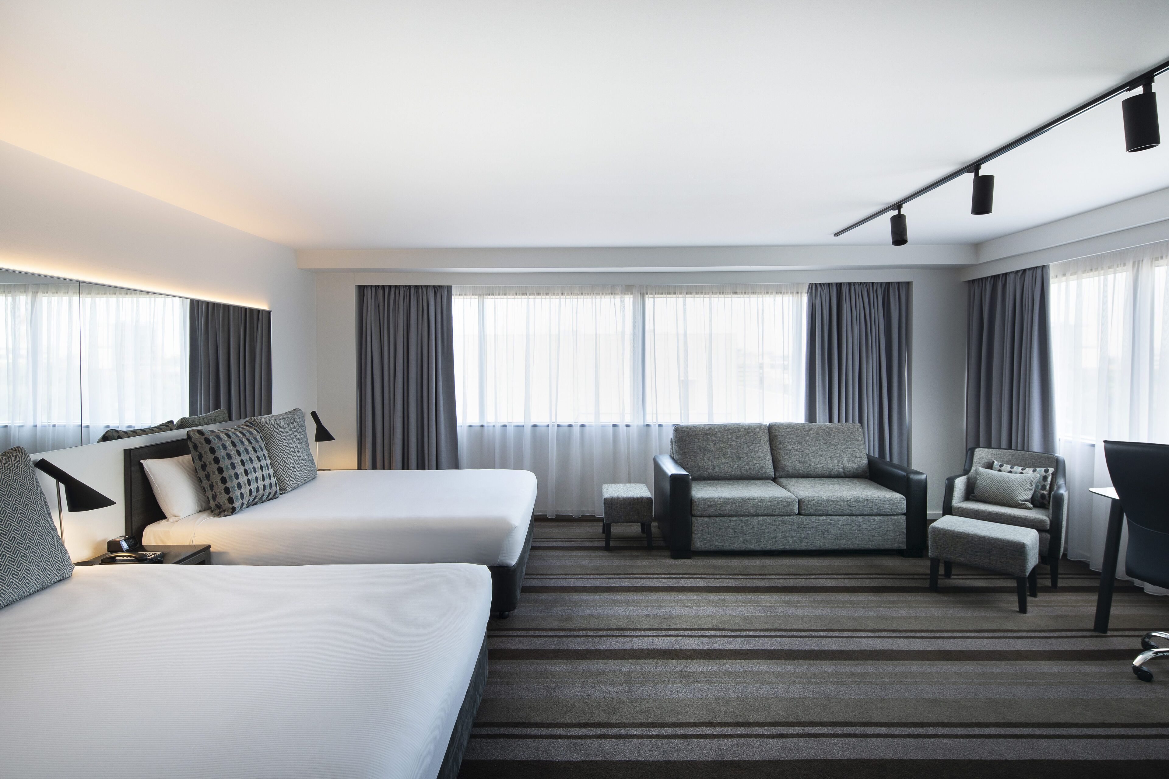 Una habitación de hotel moderna con dos camas, un sofá, una silla y un escritorio.