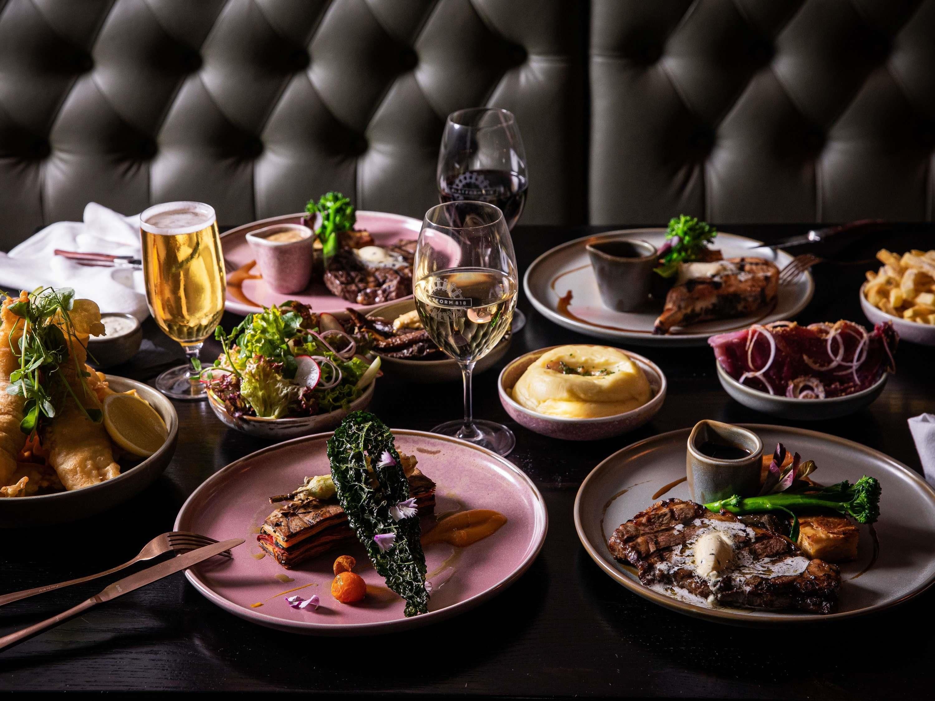 A dining table with various dishes, a glass of white wine, and a glass of beer.