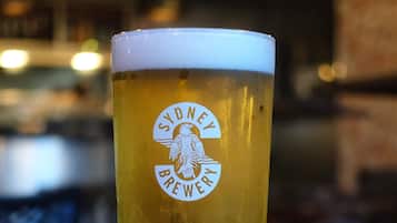A tall glass of beer with a logo, a burger, and fries on a table.