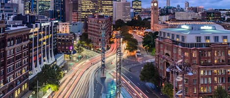 A cityscape with modern buildings, a prominent clock tower, and a busy intersection with light trails.