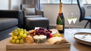 A wooden board with cheese, grapes, and crackers on a table in a modern living room with a sofa and a bottle of champagne. - Mercure Sydney (Chippendale)