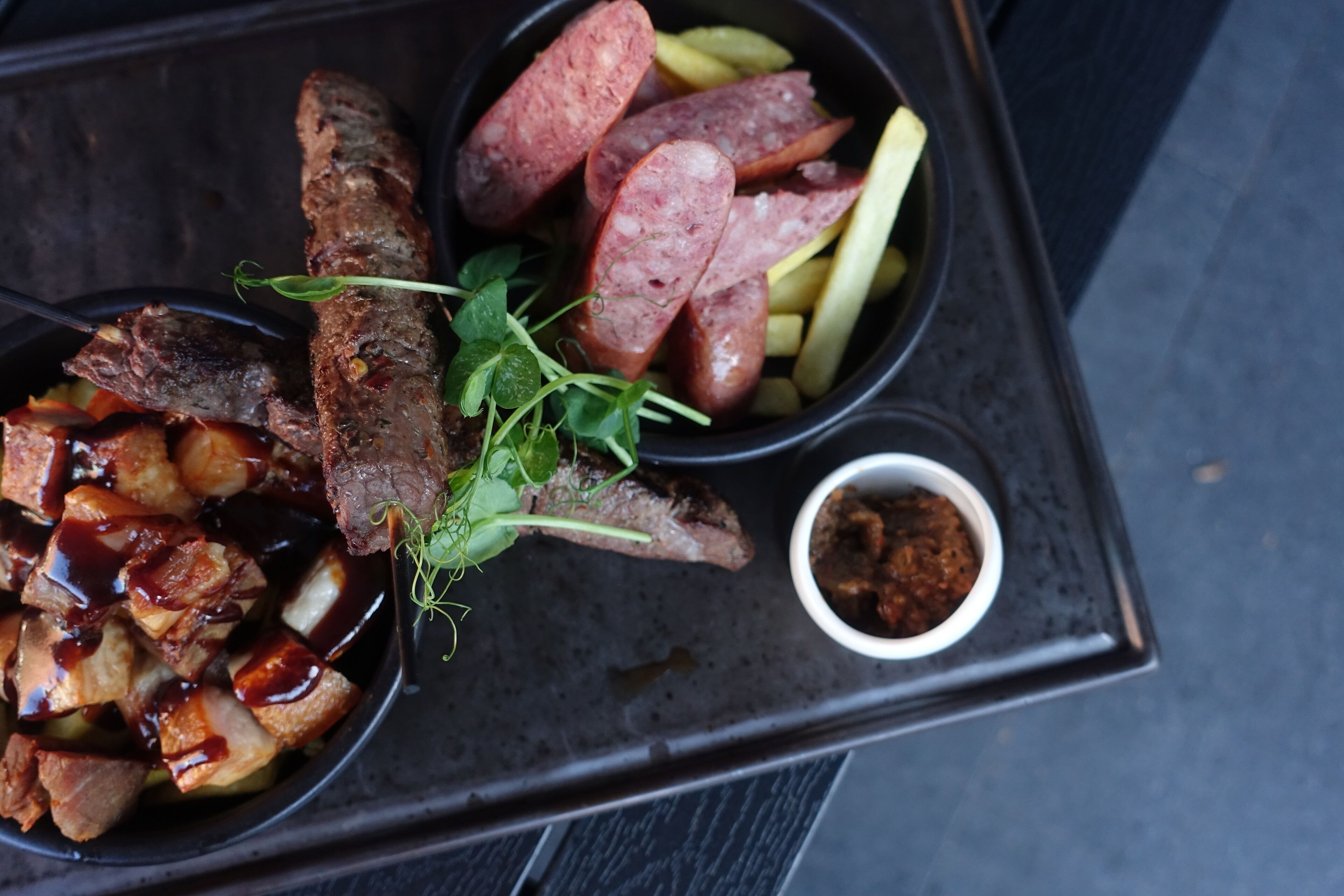 A tray with various meats, fries, and a small bowl of sauce.
