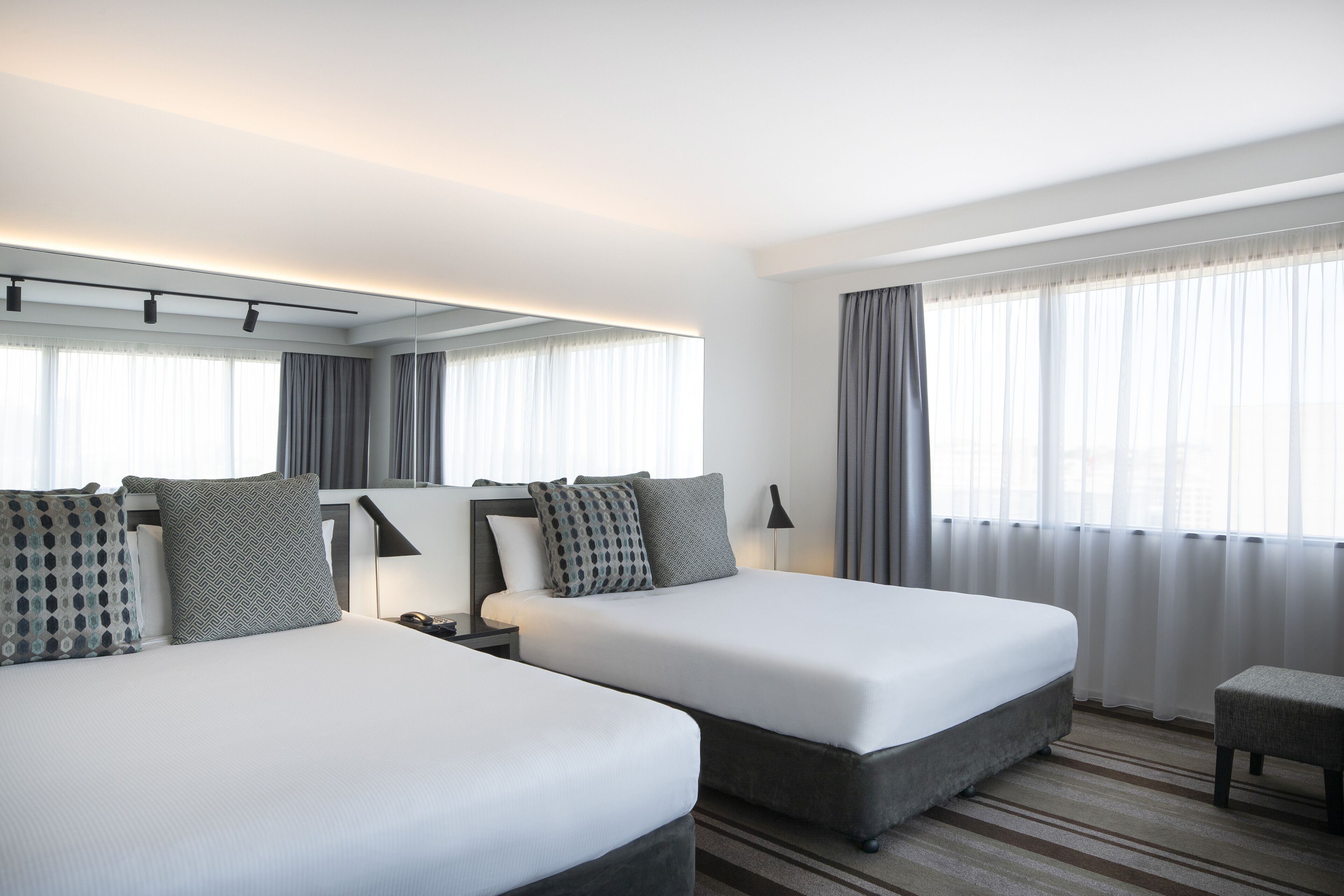 A hotel room with two beds, a nightstand, a lamp, and a window with curtains.