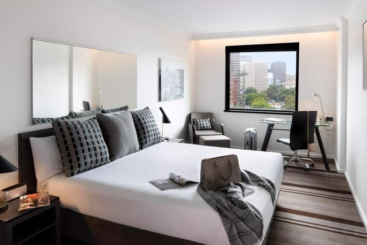 A modern hotel room with a large bed, a desk, and a chair.