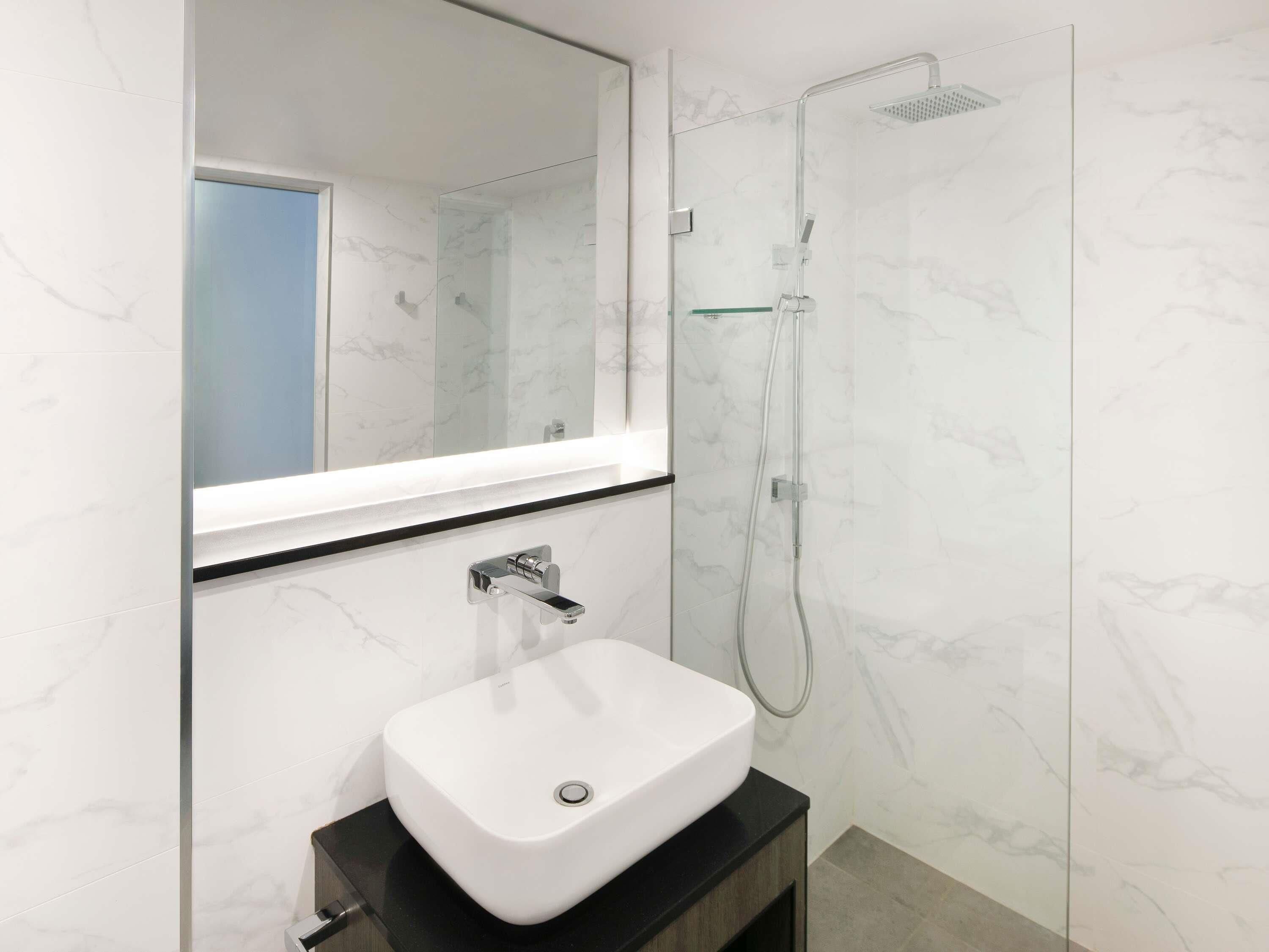 Une salle de bain moderne avec un lavabo blanc, une douche en verre et un grand miroir.