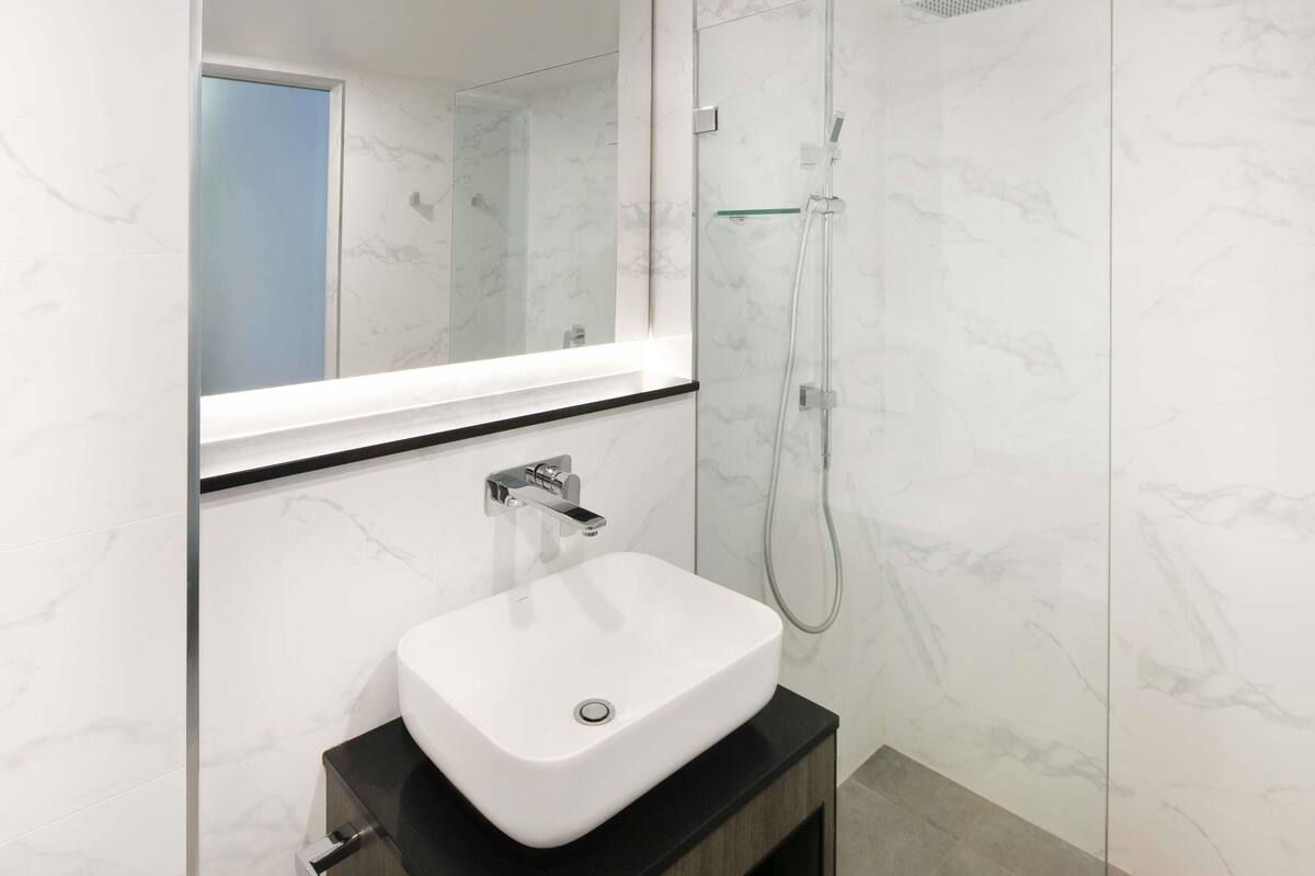 Een moderne badkamer met een wit wastafelmeubel, een douchecabine van glas en een grote spiegel.