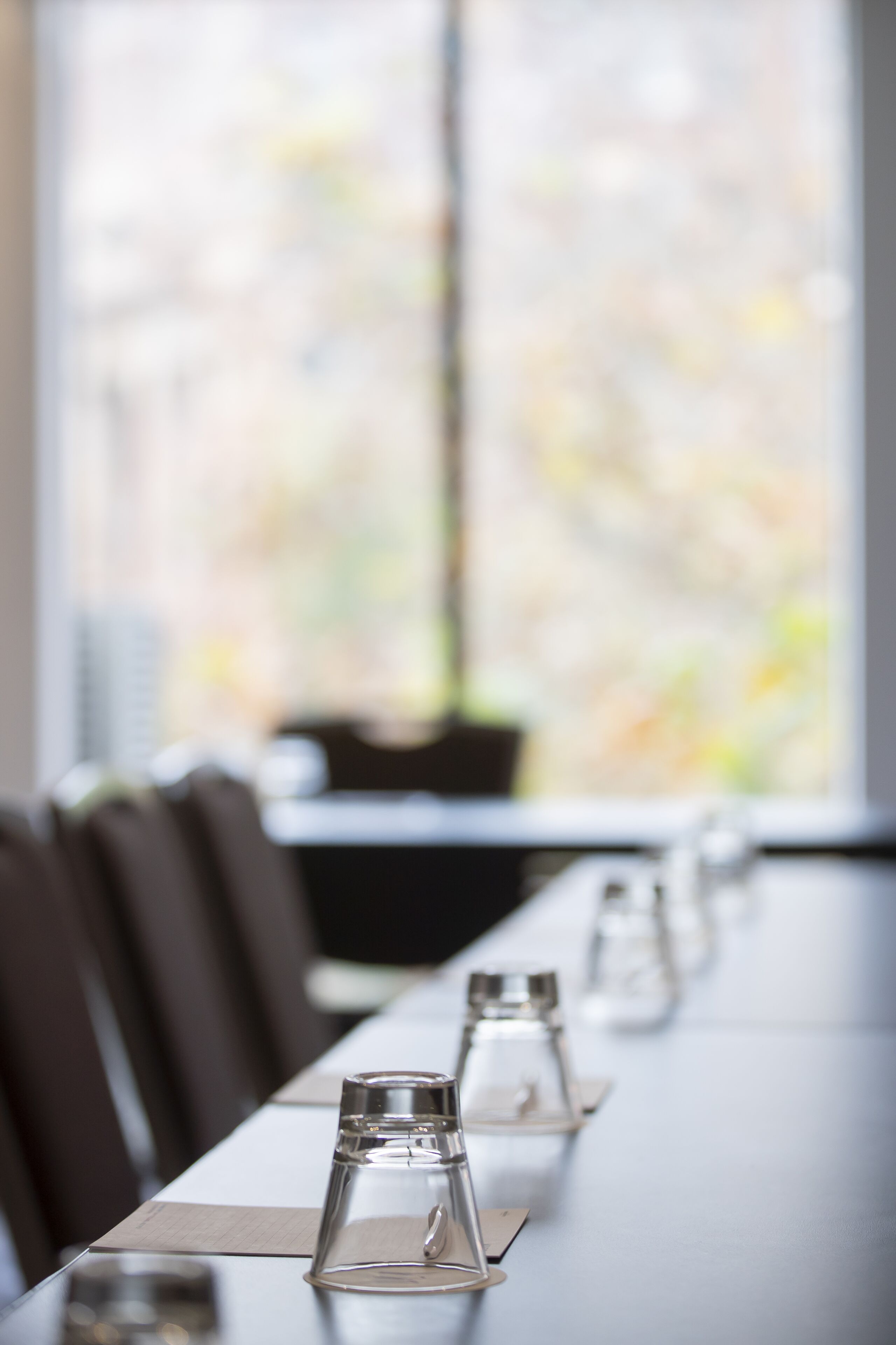 A long table with clear glass water bottles and napkins, set against a window with a blurred view of buildings.