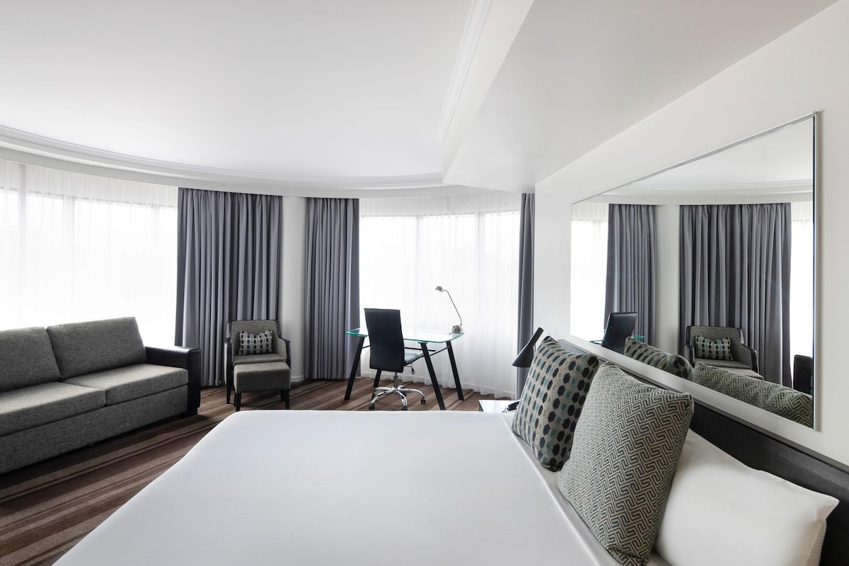 Une chambre d’hôtel avec un grand lit, un canapé, deux fauteuils, un bureau et un grand miroir.