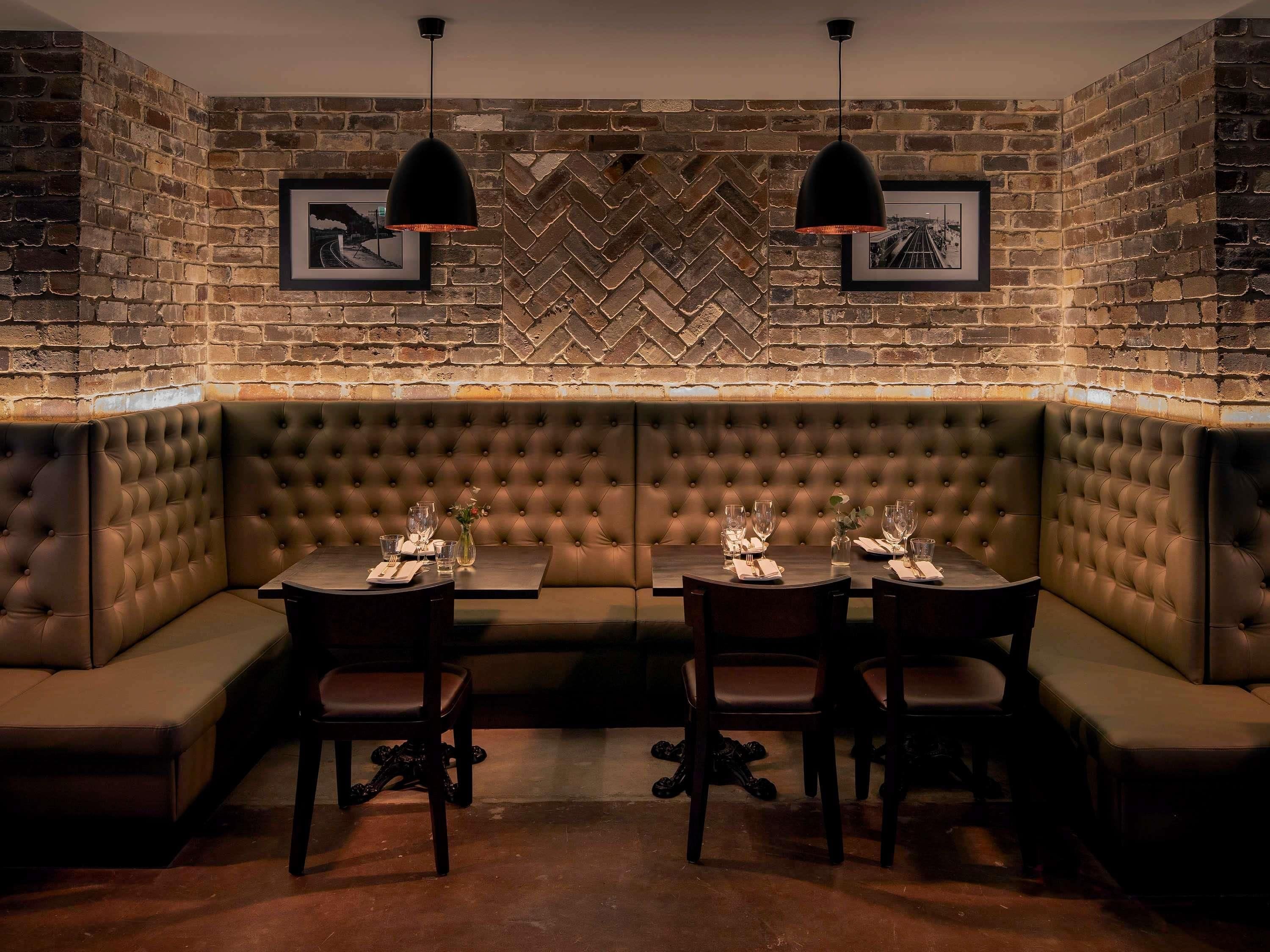 A corner seating area with a tufted bench, two tables with chairs, and pendant lighting.