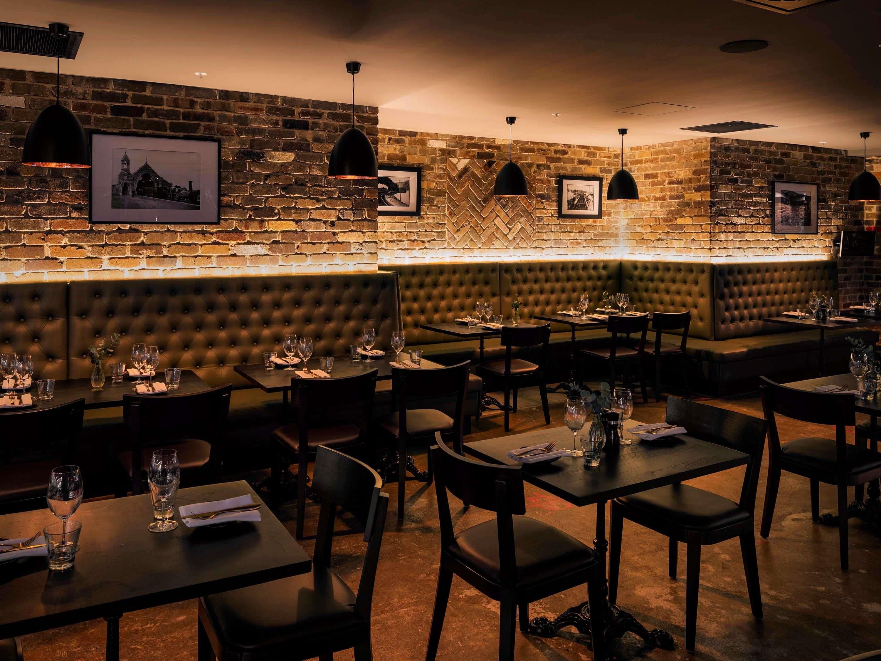 A restaurant interior with brick walls, cushioned seating, and pendant lighting.