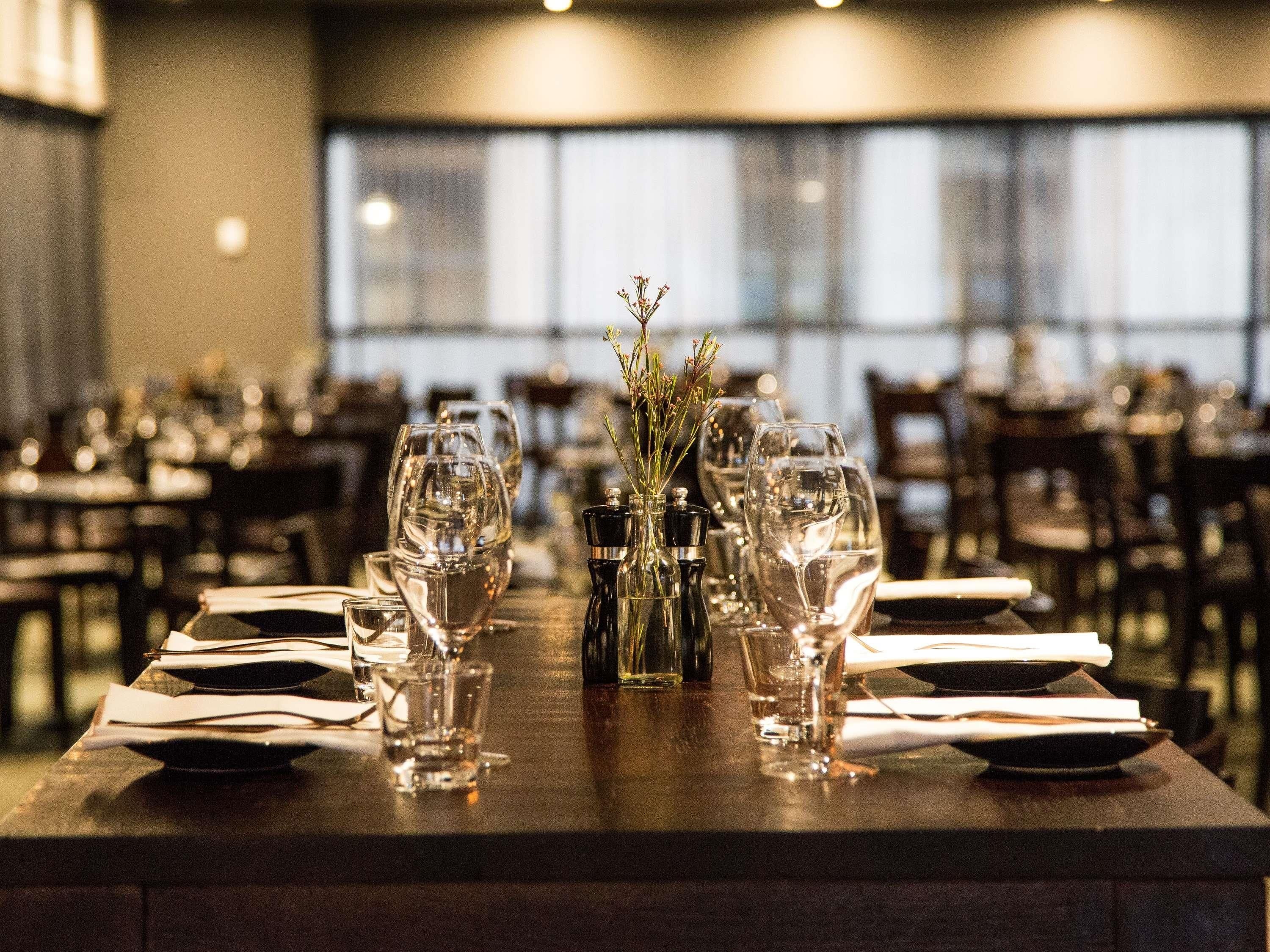 Una mesa de restaurante dispuesta con copas de vino, vasos de agua y un pequeño jarrón con plantas.