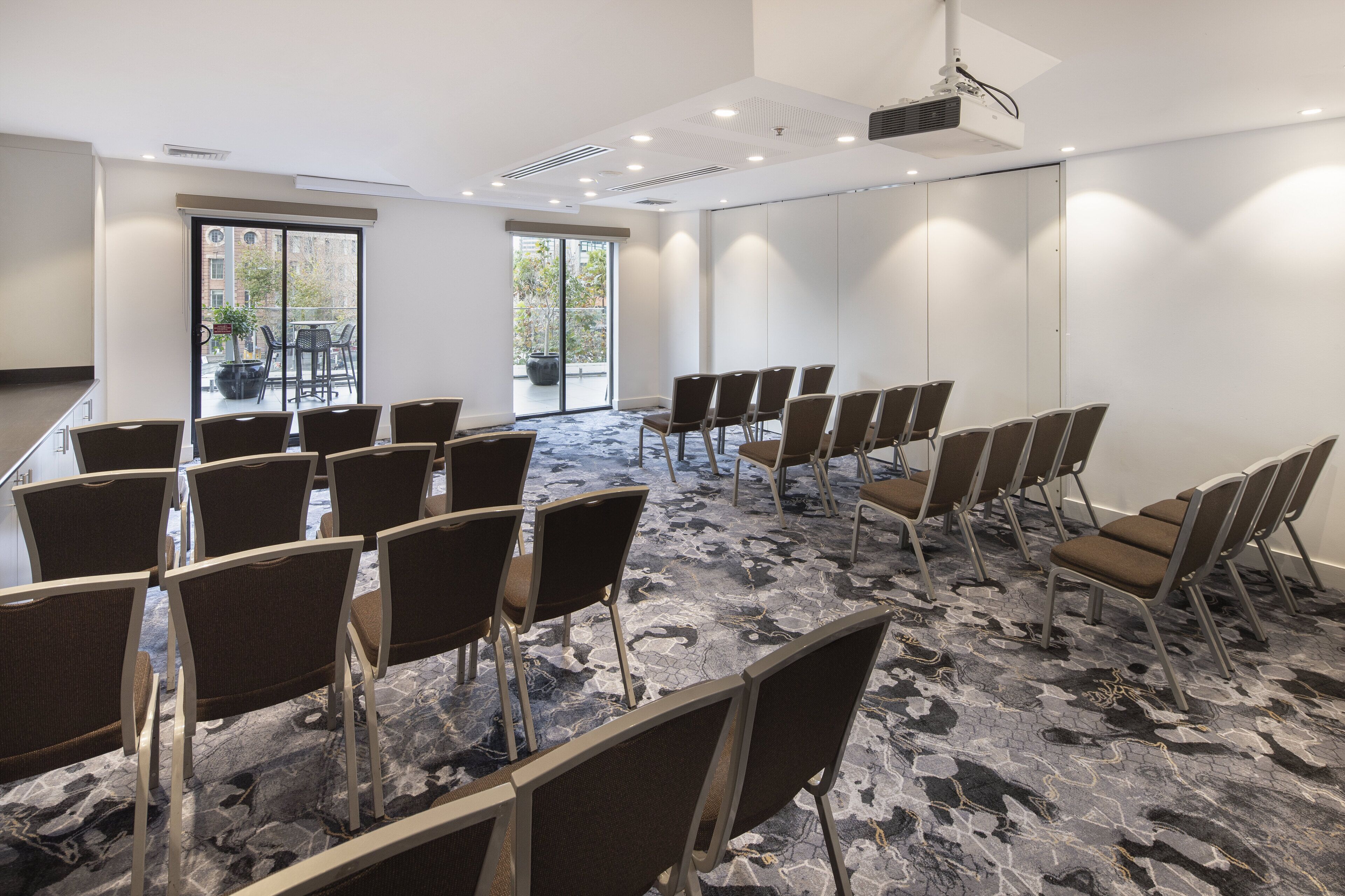 Un salón de conferencias con filas de sillas, un ventanal grande y un proyector en el techo.