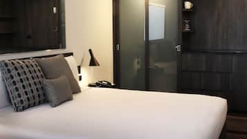 A neatly made bed with patterned pillows, a bedside lamp, a phone, and a mirror above the bed.