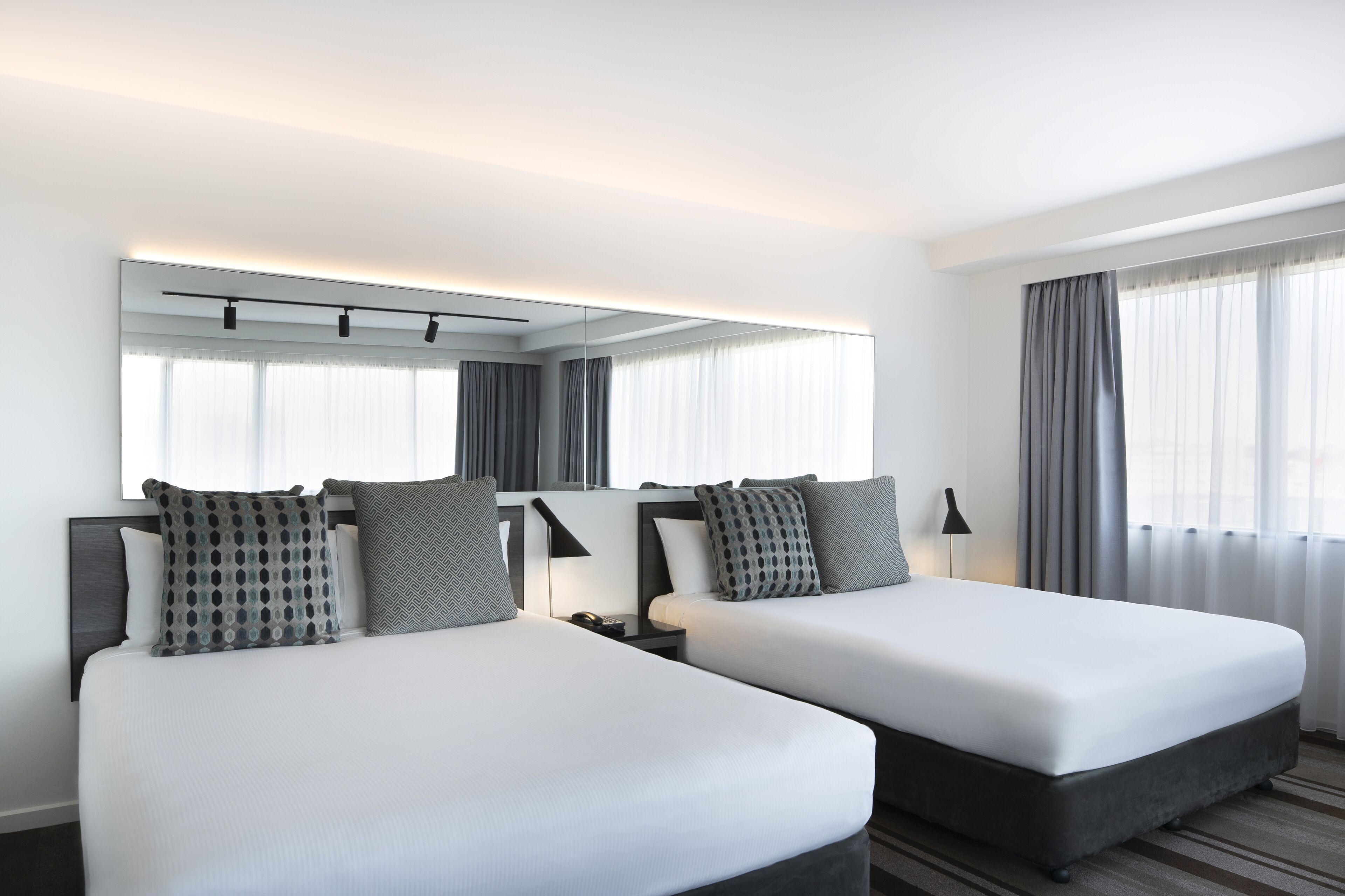 A hotel room with two beds, a large mirror, and a window with curtains.
