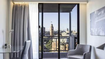 A modern hotel room with a large window, a chair, a desk, and a lamp.