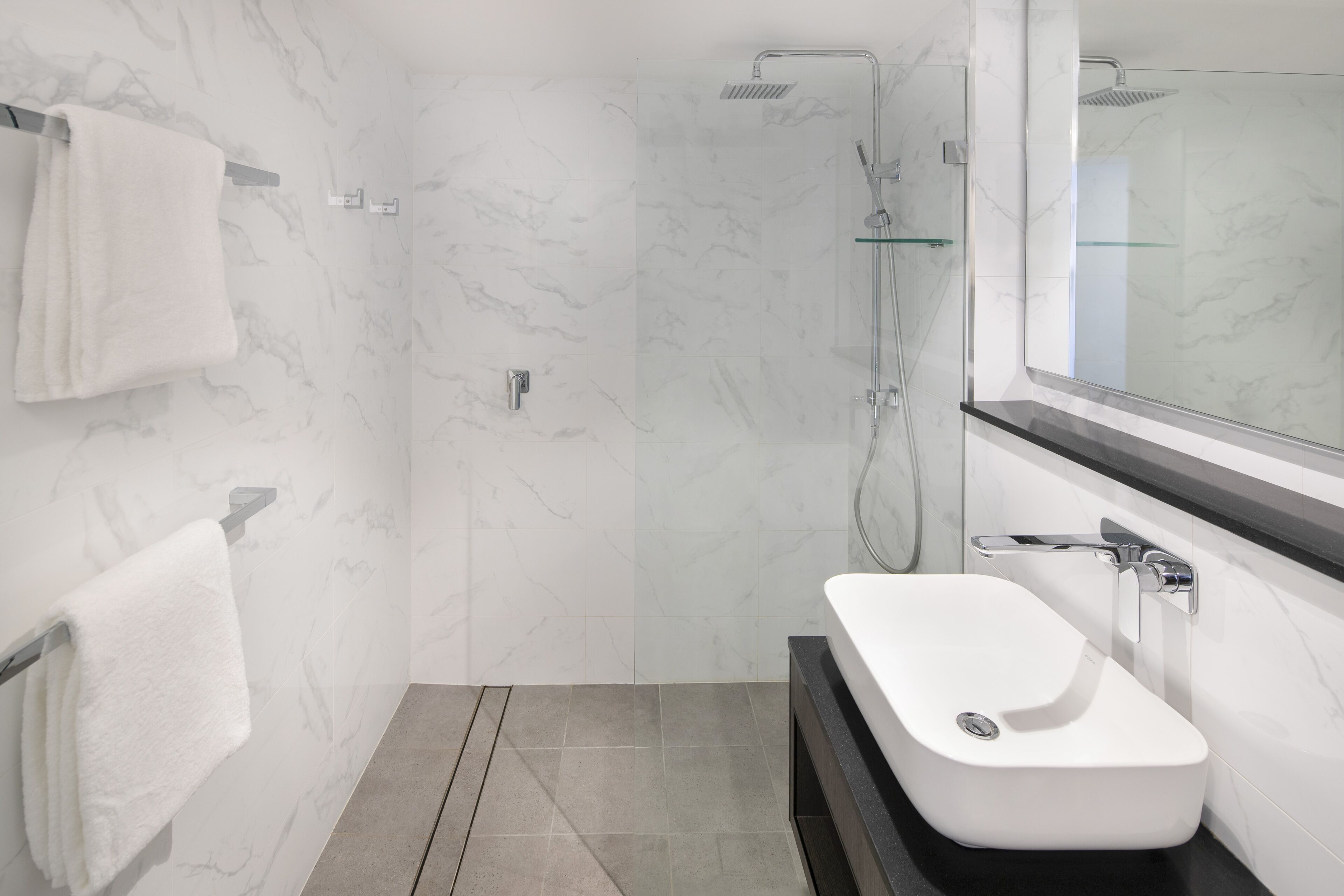 A modern bathroom with a glass shower enclosure, a white sink, and a marble-tiled shower wall.