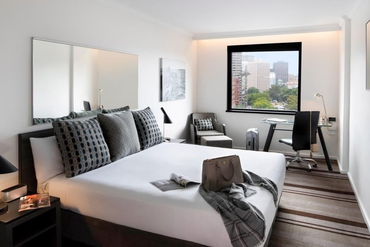 A modern hotel room with a large bed, a desk, and a chair.