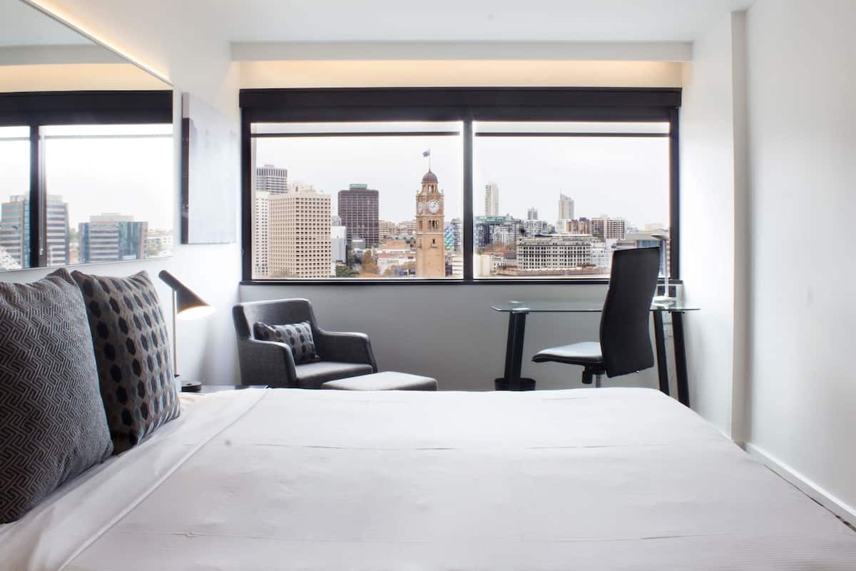 A hotel room with a large window, a bed, two chairs, and a small table.