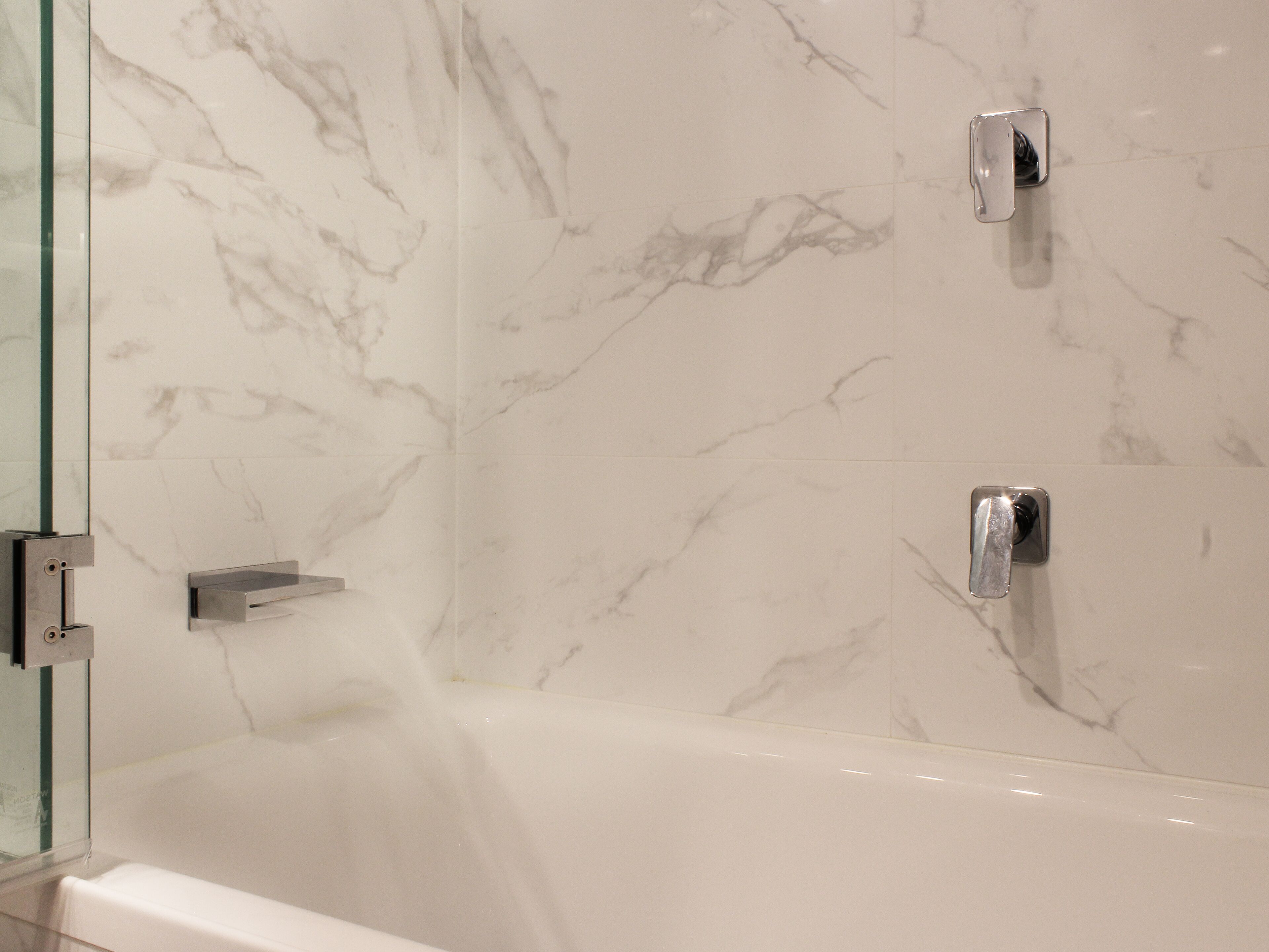 A bathroom with a marble wall, a glass shower enclosure, and a white bathtub.