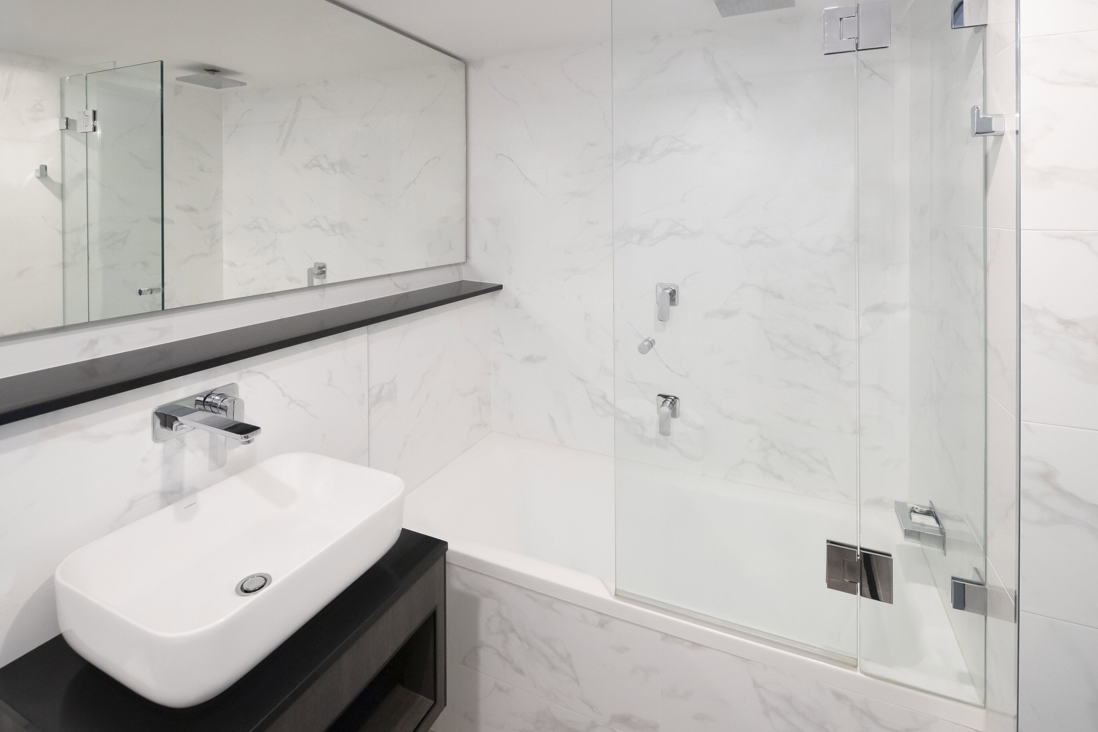 A modern bathroom with a white sink, a glass-enclosed shower, and a marble-tiled wall.