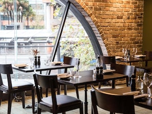 An indoor dining area with brick walls, large windows, and tables set for dining.