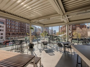 A covered outdoor seating area with tables and chairs, large windows, and a view of the cityscape. - Mercure Sydney (Chippendale)