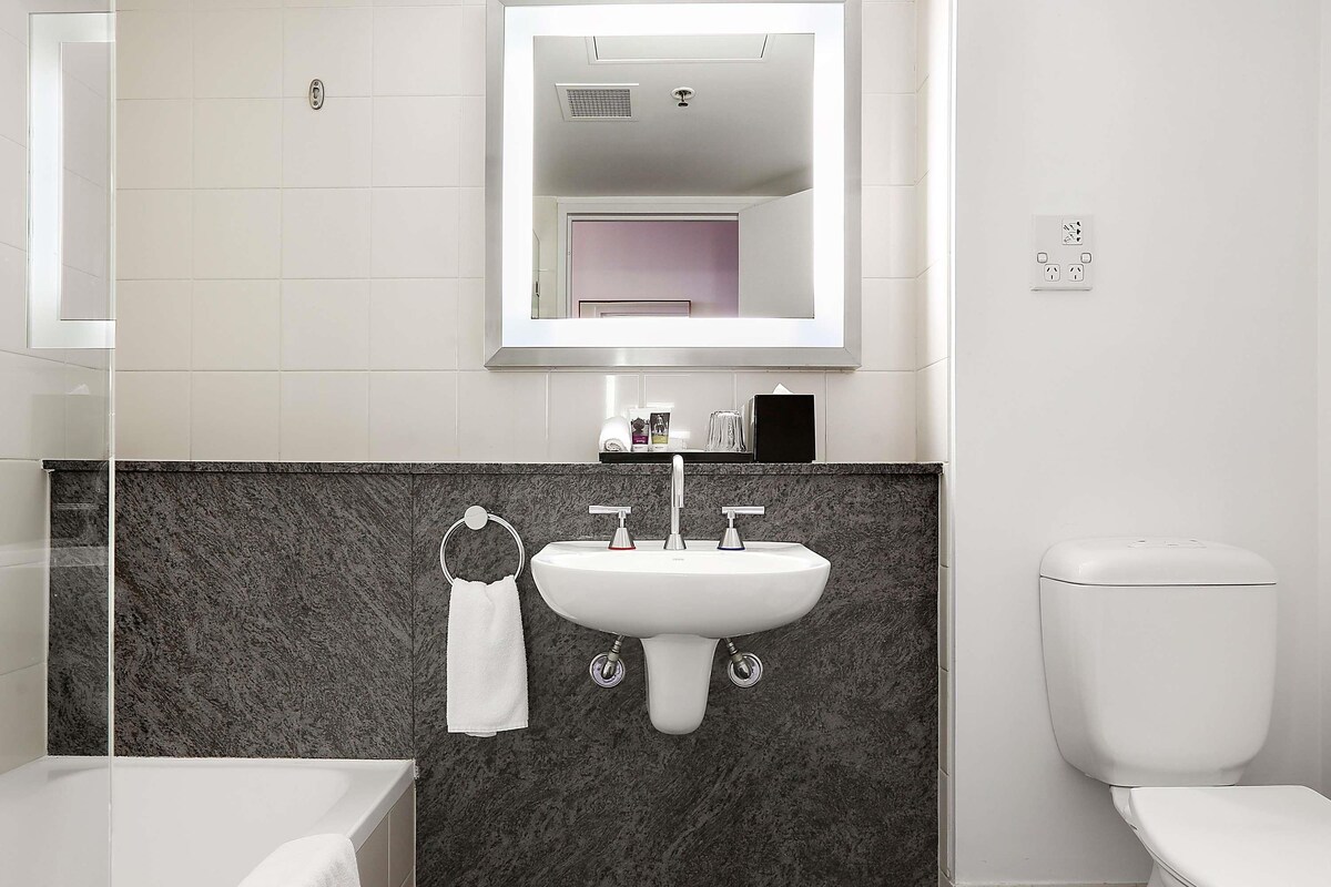 A modern bathroom with a white sink, dark marble backsplash, a white toilet, and a glass-enclosed shower.