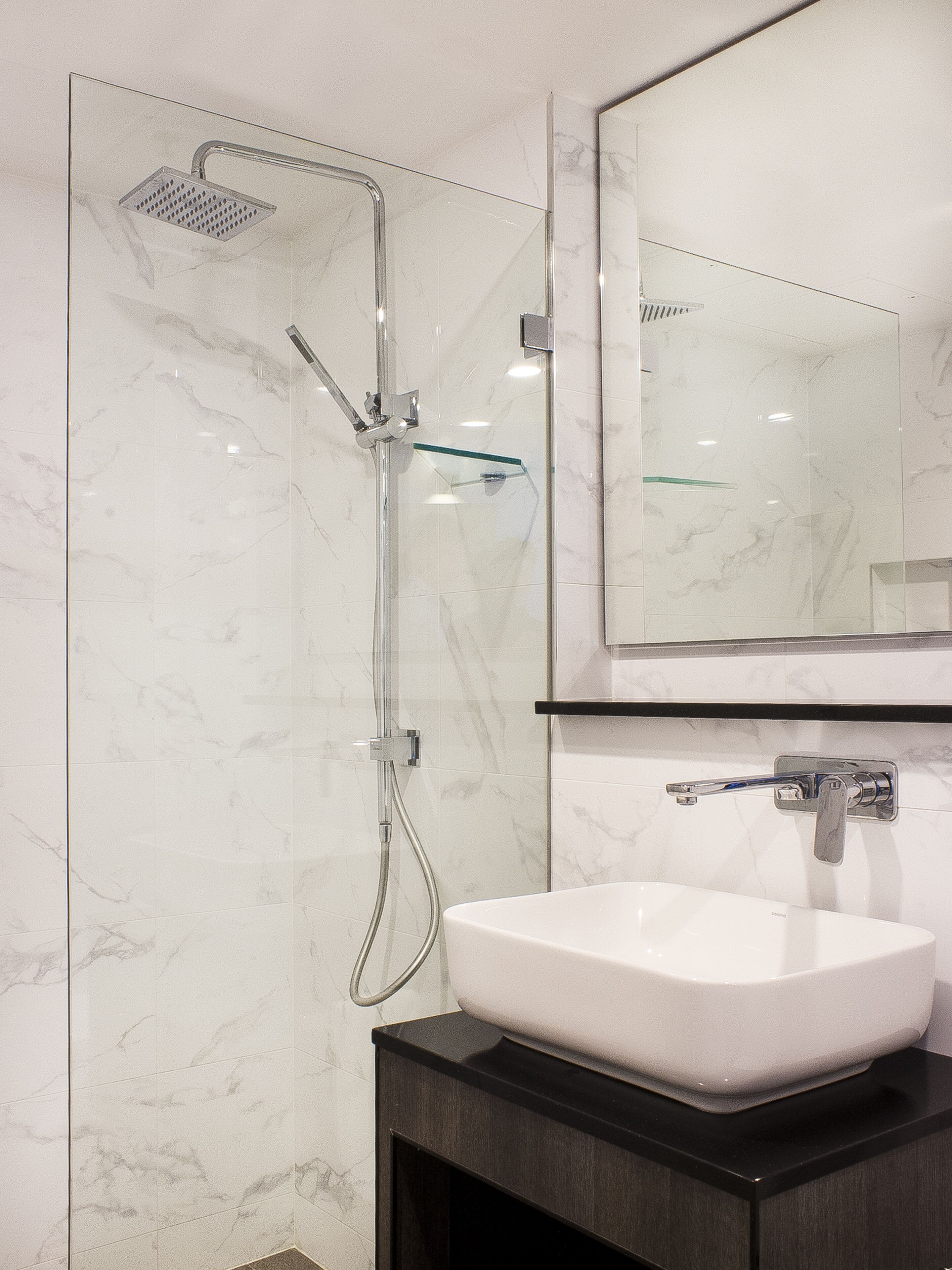 A modern bathroom with a glass-enclosed shower, a white sink, and a large mirror above the sink.