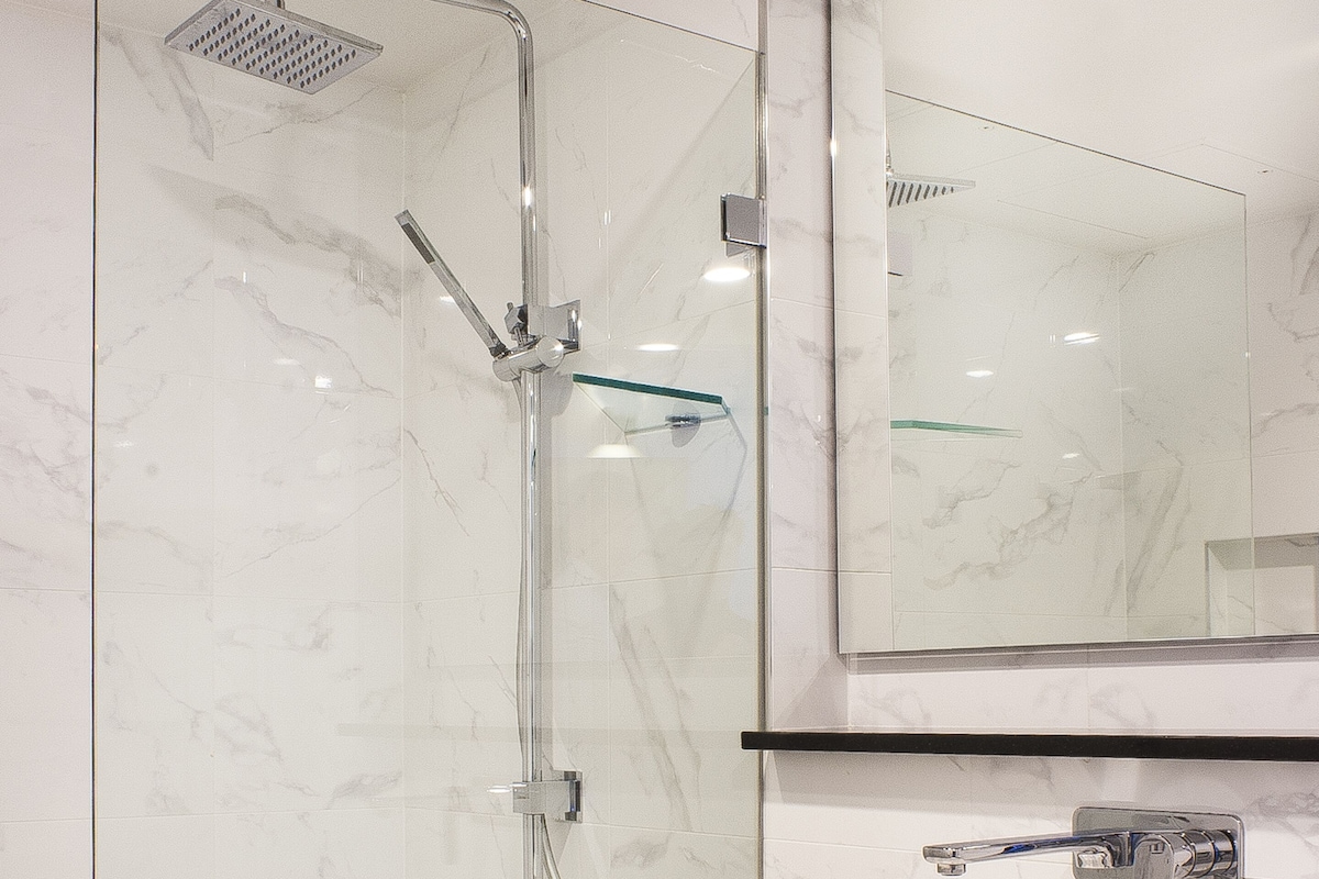 Une salle de bain moderne avec une douche à parois de verre, un lavabo blanc et un grand miroir au-dessus du lavabo.