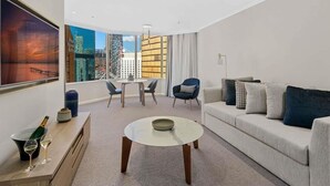 A modern living room with a sofa, a coffee table, a dining table with chairs, and a large window with a city view.
