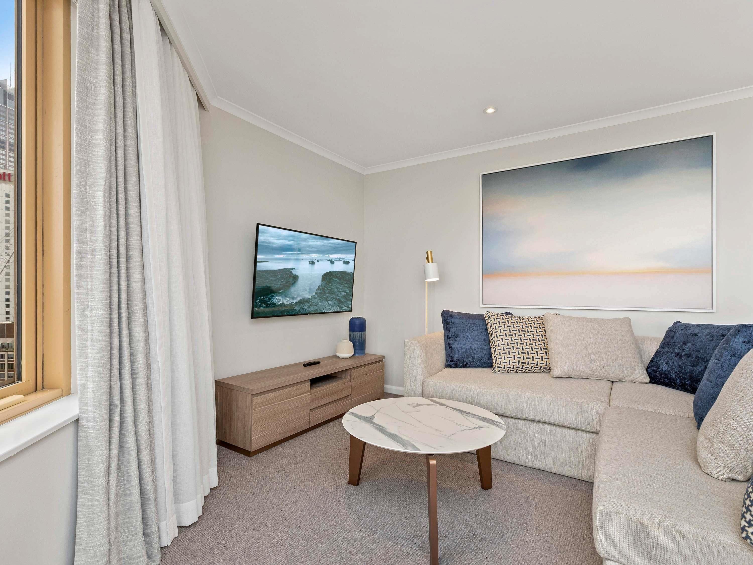 A modern living room with a sofa, a small table, a TV, and artwork on the wall.