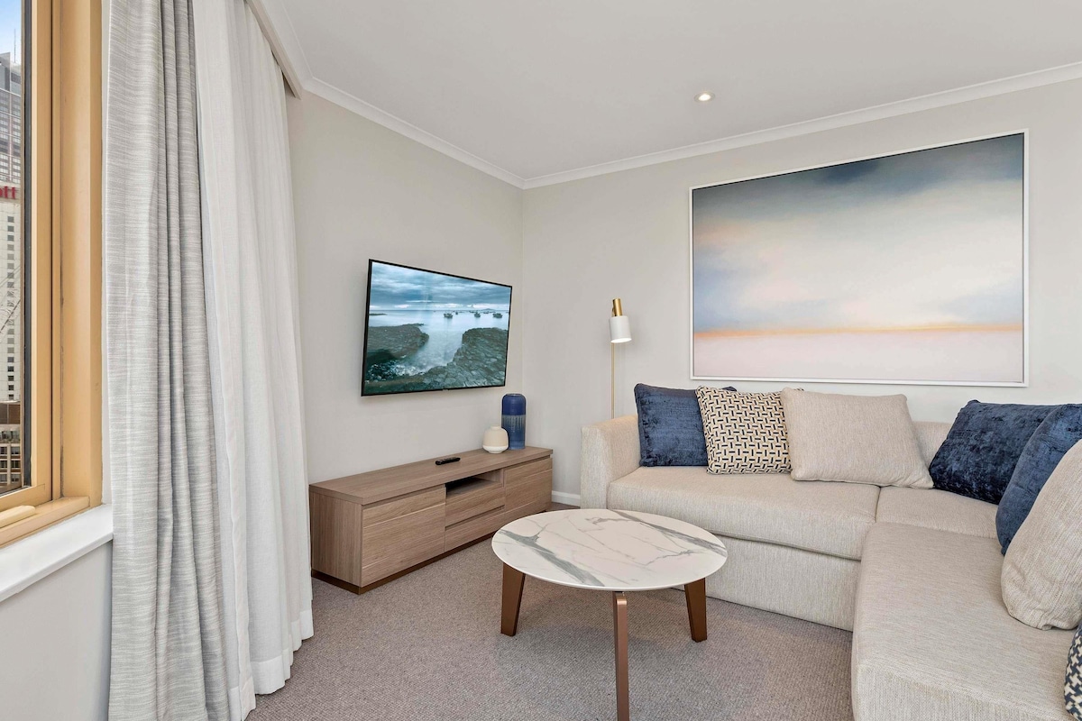 A modern living room with a sofa, a small table, a TV, and artwork on the wall.