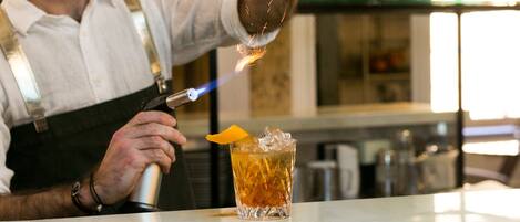 A bartender preparing a drink with a torch, surrounded by shelves of bottles and glasses.