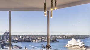 A dining area with a table set for four, large windows offering a view of a city skyline and a famous opera house.