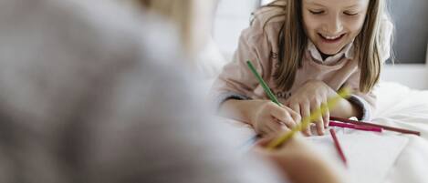 A person sitting at a table with various colored pencils and a notebook.