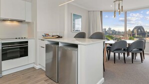 A modern kitchen with a built-in oven and refrigerator, a dining area with a table and chairs, and a large window offering a city view.