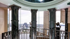 A balcony with a view of the Sydney Harbour Bridge, featuring large columns and a glass railing.