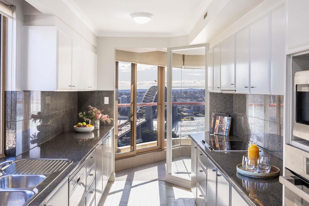 A modern kitchen with white cabinets, granite countertops, and a large window offering a city view.