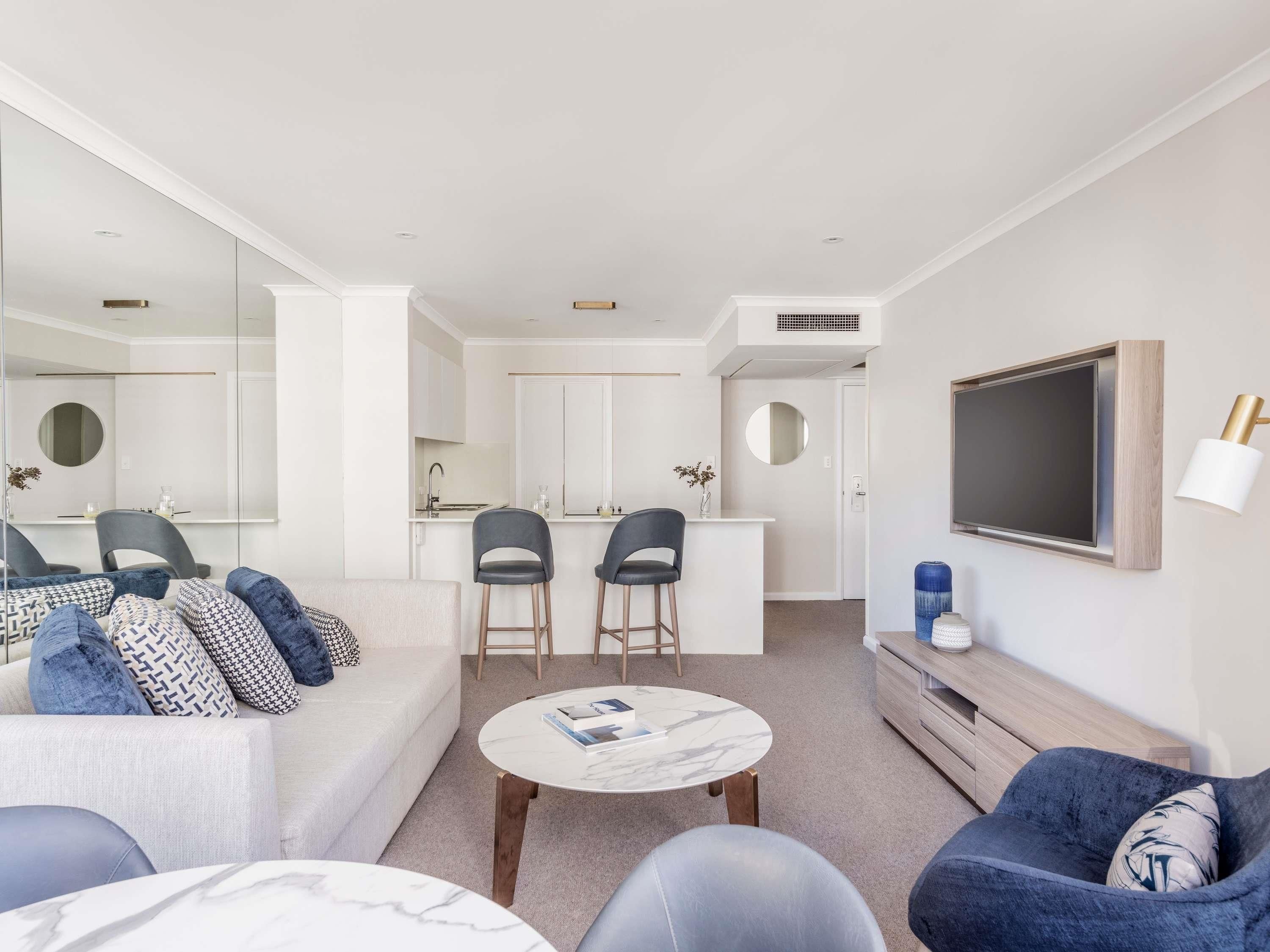 A modern living room with a sofa, two chairs, a coffee table, and a TV mounted on the wall.