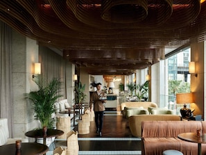 A hotel lobby with a central seating area, a reception desk, and large windows offering views.
