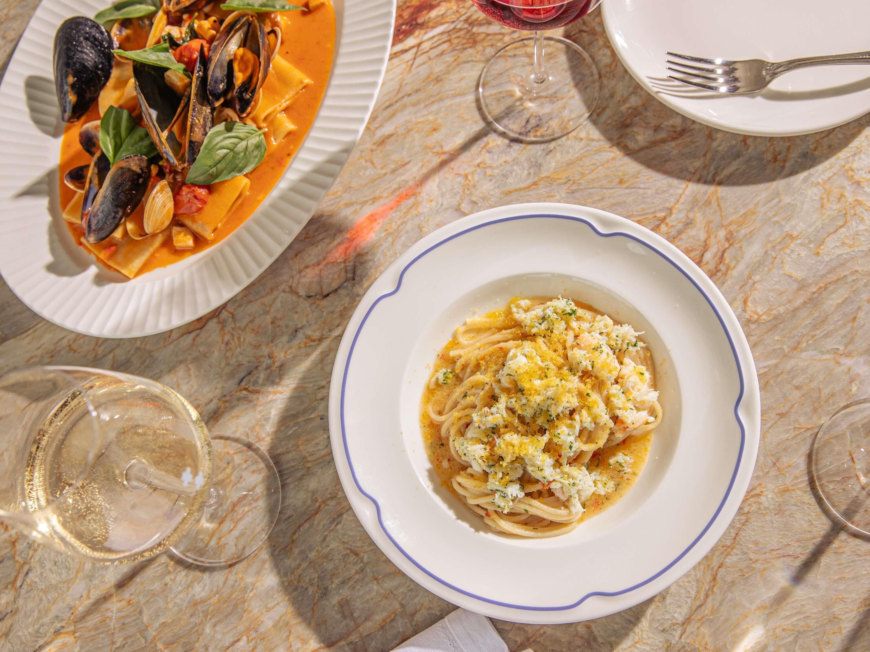 Una mesa de comedor con dos platos de pasta, una copa de vino y un tenedor.