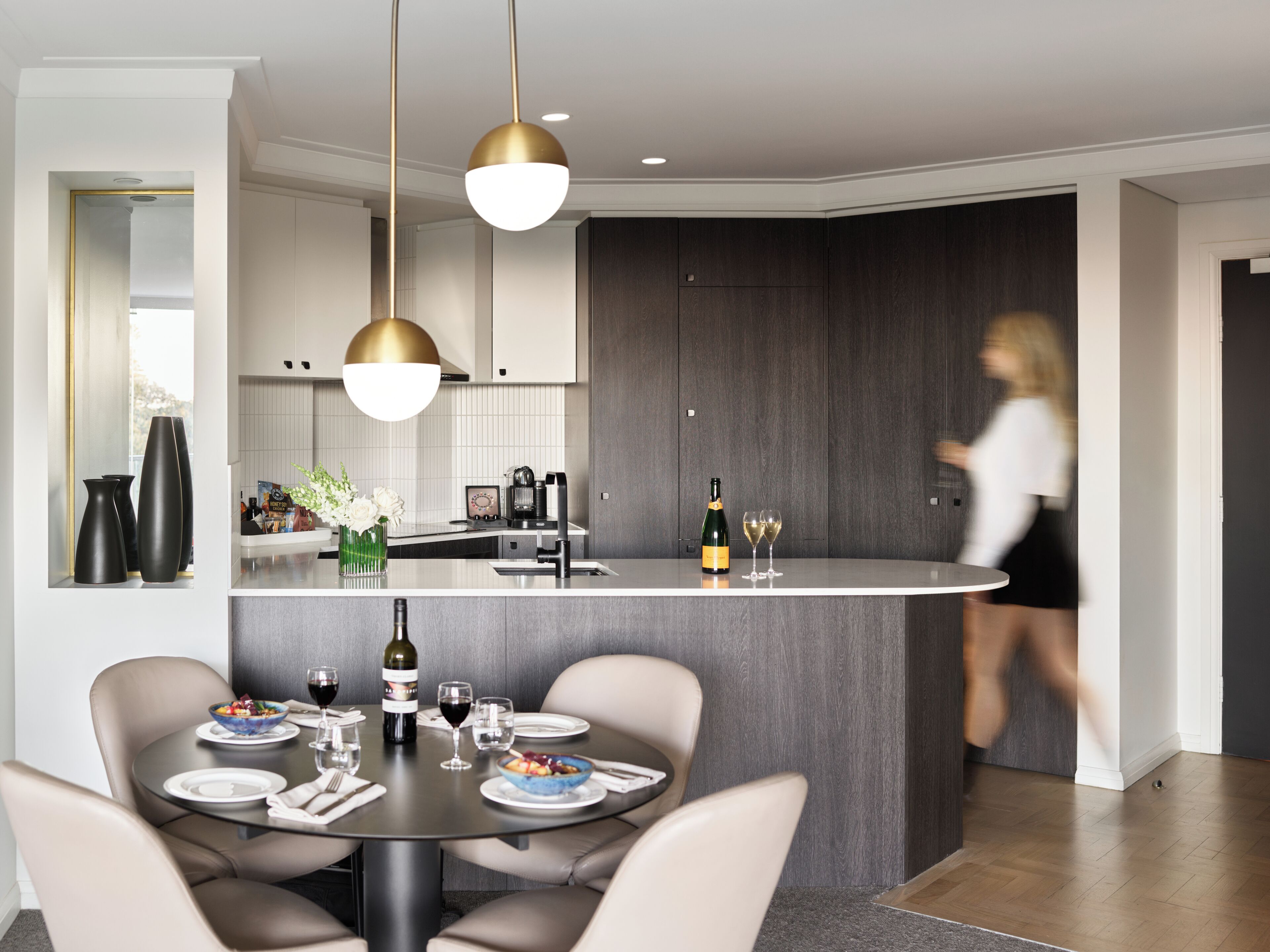 A modern kitchen with a central island, pendant lighting, and a dining area with a round table and chairs.