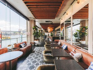 A spacious indoor seating area with leather sofas, round tables, and potted plants. - Pullman Quay Grand Sydney Harbour (Sydney)